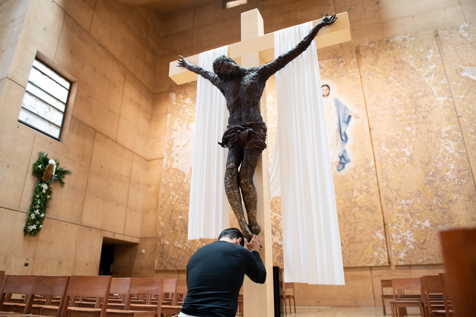 Bronze crucifix above a kneeling visitor