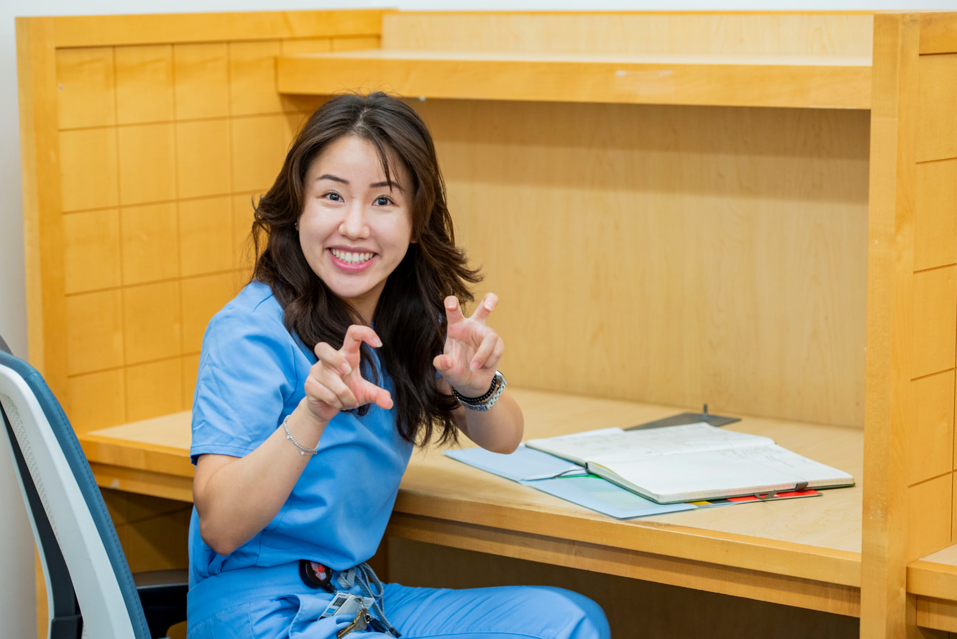Nurse in blue scrubs smiling at a desk